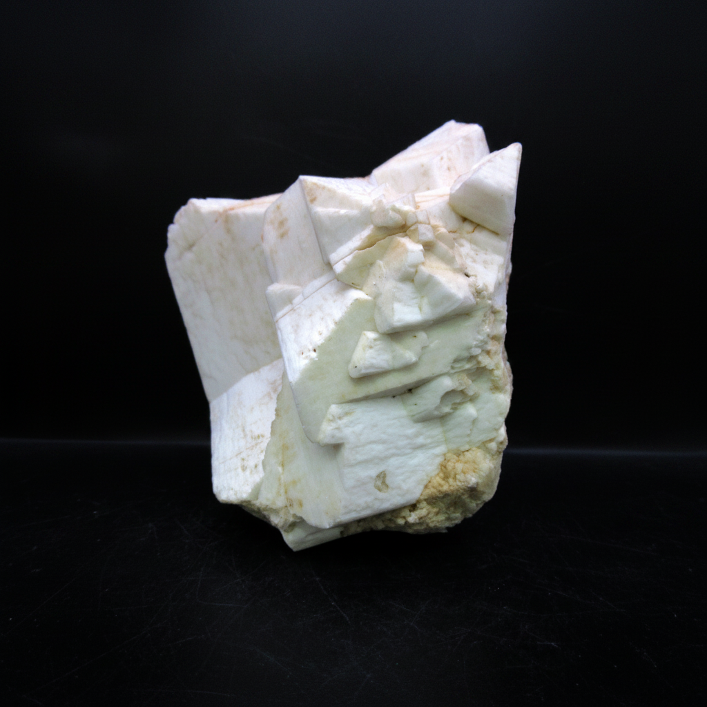 White Feldspar mineral specimen displaying characteristic stepped cleavage faces and pale green tones against a solid black background